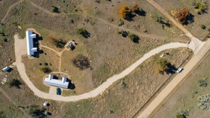 An aerial view of a property with a winding road, a large building with a flat roof, and several smaller structures. - Holy Cow Cottage w/Amazing Hill Country Views (Fredericksburg)
