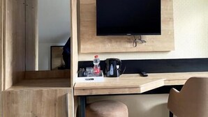 Una camera d'albergo moderna con una scrivania in legno, una TV a schermo piatto fissata al muro, un poggiapiedi e una sedia.