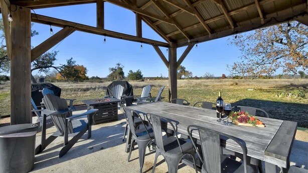 Eine überdachte Terrasse im Freien mit Holztisch und -stühlen, einem Grill und einer reizvollen Aussicht auf die Landschaft.