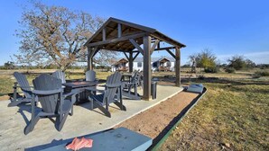 An outdoor patio with Adirondack chairs and a table, a wooden pergola structure, and a house in the background. - Bonny Bluebonnets Cottage w/Stunning Hill Country (Fredericksburg)