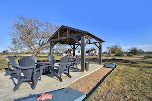An outdoor patio with Adirondack chairs and a table, a wooden pergola structure, and a house in the background.