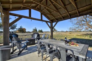 Eine Terrasse im Freien mit Holztisch und Stühlen, einem Grill und einer Weinflasche.