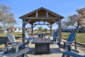 Eine Außenpatio mit Adirondack-Stühlen, einem Holz-Pavillon und einer Feuerstelle.