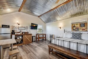 Una habitación acogedora y luminosa con una mesa de madera, un sofá y una zona de cocina con microondas y armarios.
