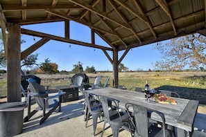 An outdoor patio with a wooden table and chairs, a grill, and a bottle of wine.