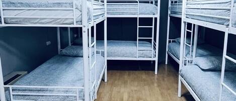 A room with three bunk beds aligned in a row, wooden flooring, and a ceiling light.
