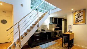 A modern kitchen with a glass staircase, wooden flooring, and a dining area with a table and chairs.