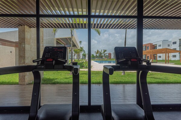 Two treadmills with digital displays, a wooden deck, and a view of a swimming pool and buildings.