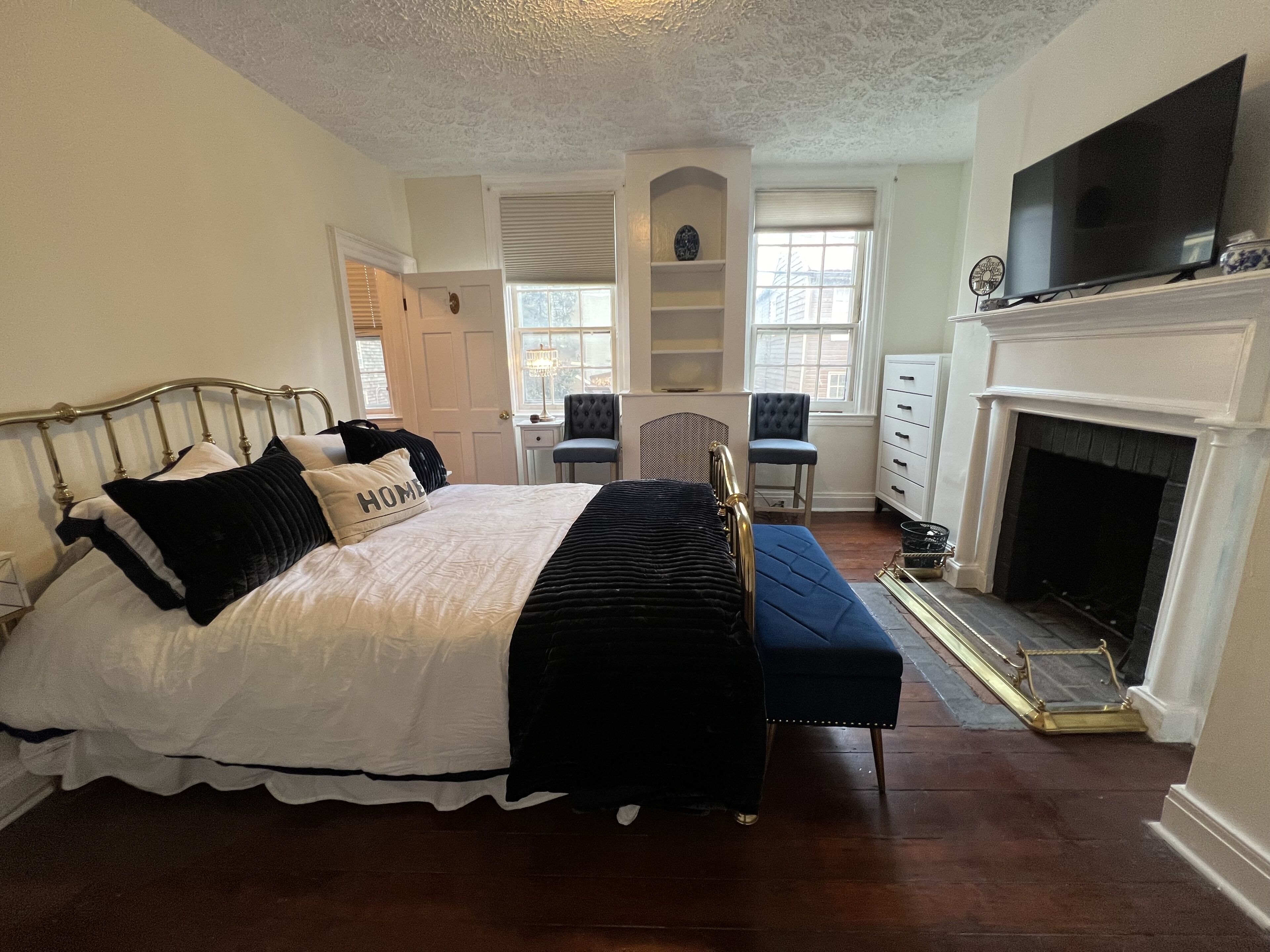 A bedroom with a bed, two chairs, a dresser, a television, and a fireplace.