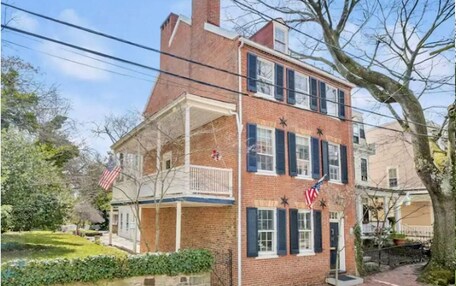 A two-story brick building with a balcony, American flags, and a stone wall.
