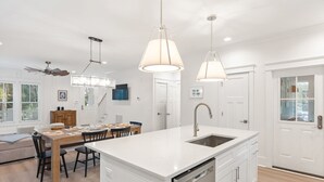 Una cocina moderna con una isla central, armarios blancos e iluminación colgante.