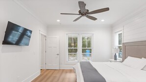 Un dormitorio con cama, ventilador de techo, televisor montado en la pared y ventana con persianas.