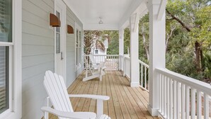 Un porche cubierto con barandillas blancas, piso de madera y dos sillas Adirondack blancas.