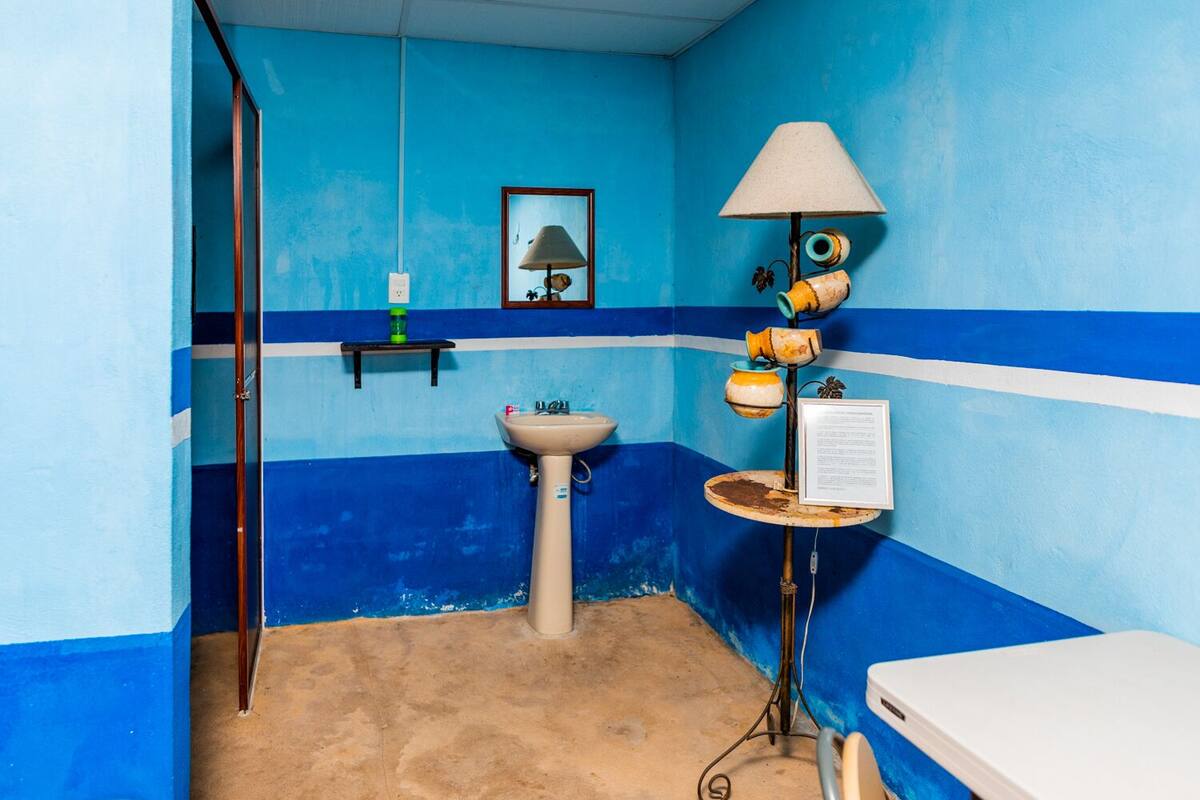 A bathroom with a sink, a mirror, a shelf with toiletries, and a toilet.
