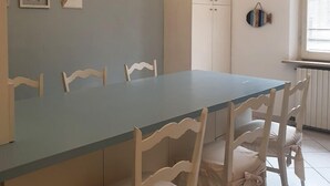 A dining area with a long table and white chairs, a cabinet, and wall decorations. - Cleo Tulipano (Falconara Marittima)