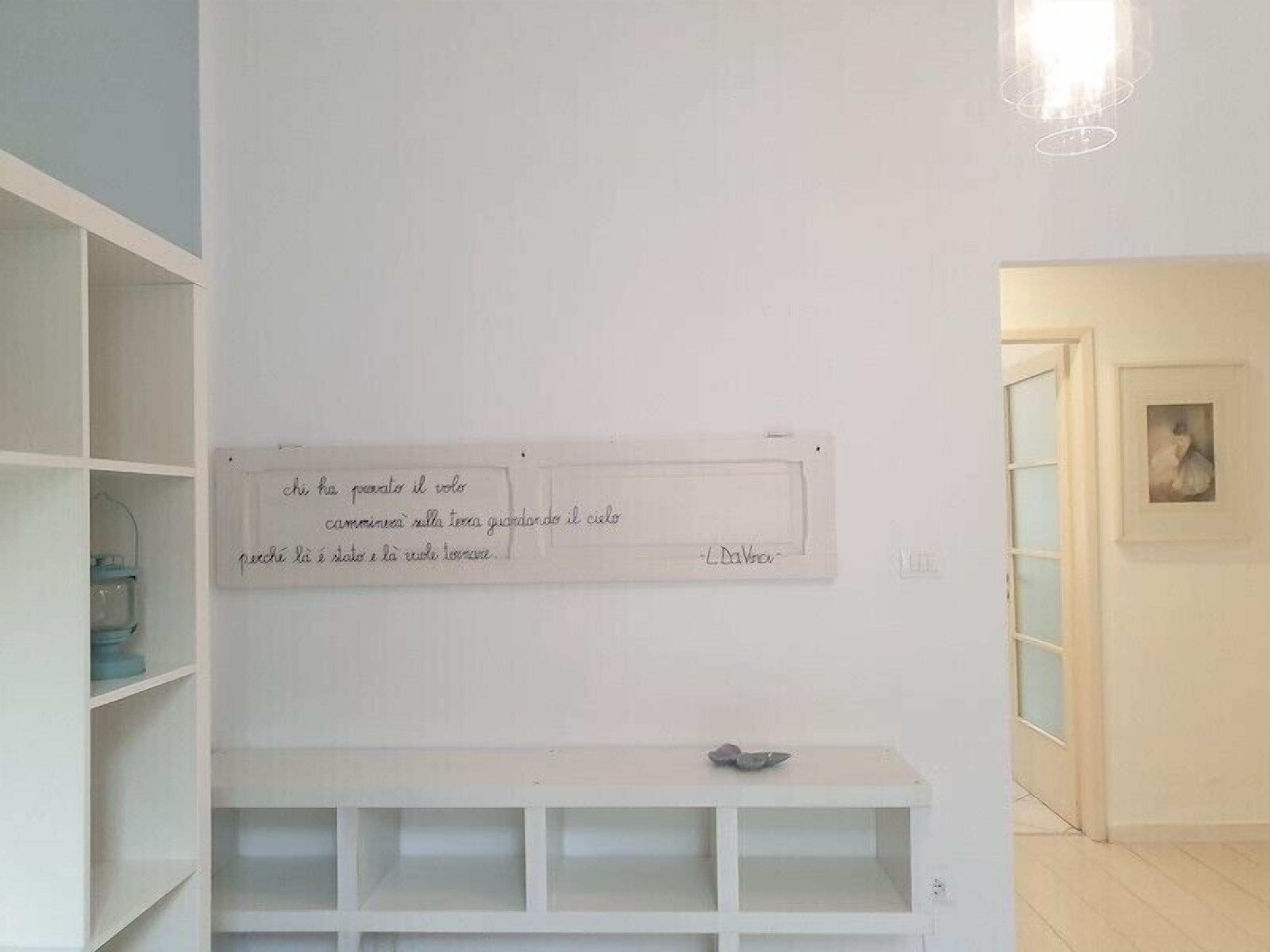A minimalist room with white walls, a white shelf unit, and a framed text on the wall.