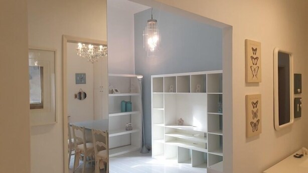 A modern, minimalist room with white walls, a chandelier, and built-in shelving. - Cleo Tulipano (Falconara Marittima)