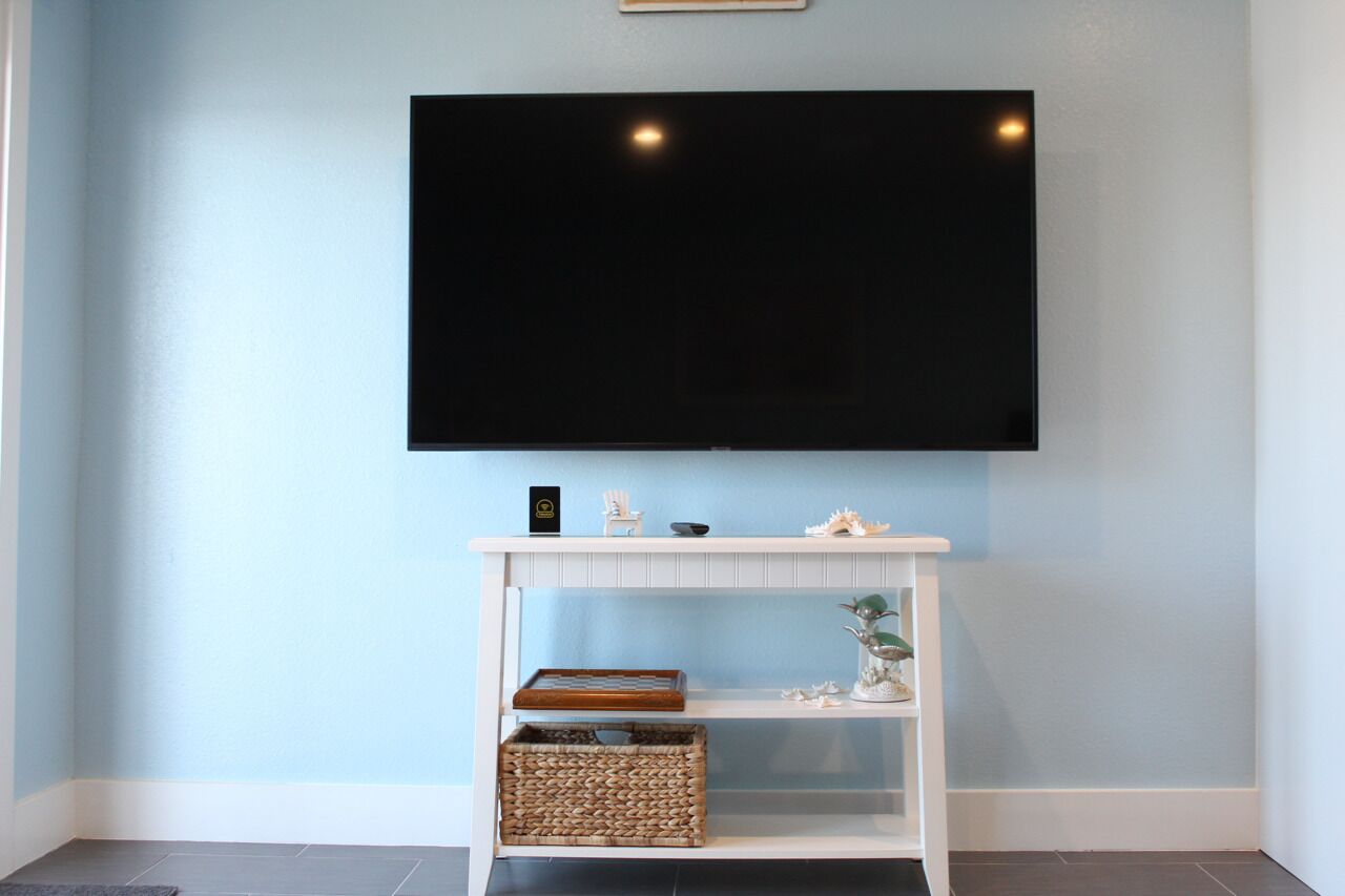 Een flatscreen televisie bevestigd aan een muur boven een witte console met planken en manden.