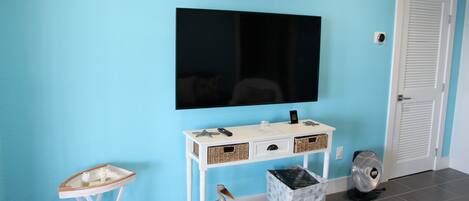A room with a blue wall, a white console table with baskets, a small white table, a television, and a door with a sign.