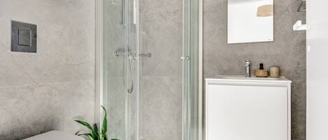 A modern bathroom with a glass-enclosed shower, a white toilet, a sink with a mirror, and a potted plant.