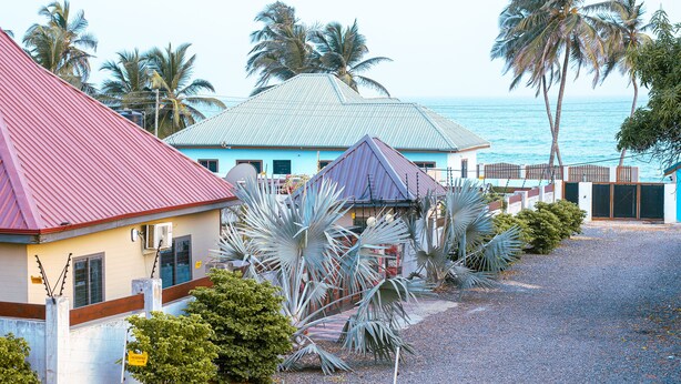 A coastal property with a red-roofed building, a blue building with a grey roof, and a view of the ocean. - Afua Oparebea Courts (Prampram)