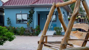 A wooden swing set in a garden area with a blue house in the background. - Afua Oparebea Courts (Prampram)