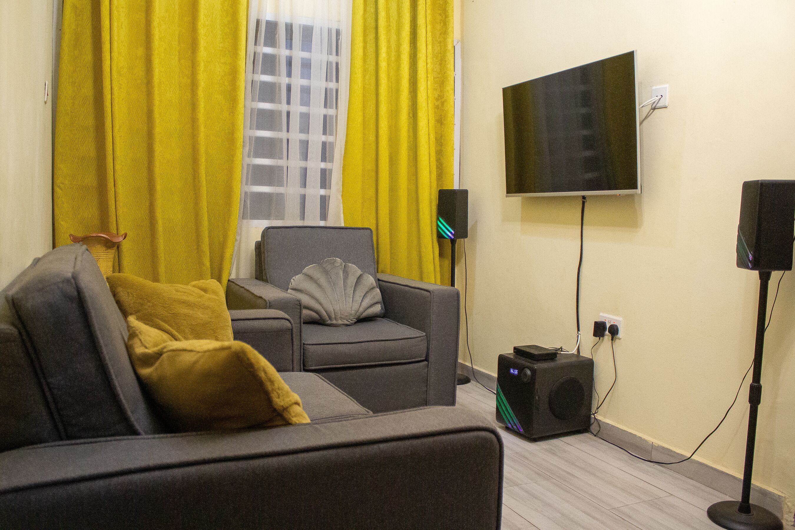 A modern living room with a sofa, a chair, a flat-screen TV, and a speaker system.