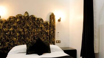 A hotel room with a patterned headboard, a bed with white and black bedding, a black pillow, a nightstand, and a black curtain.