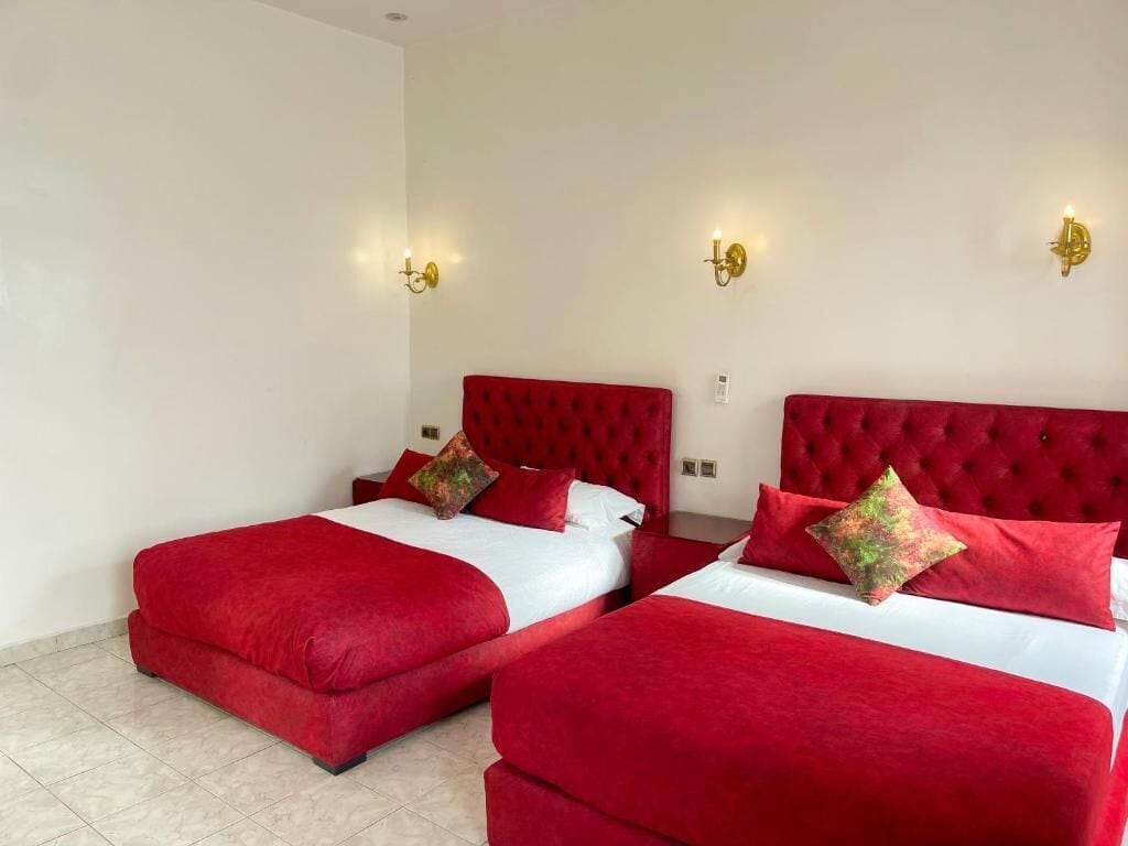 Habitación de hotel con dos camas rojas, ropa de cama blanca y apliques dorados en la pared.