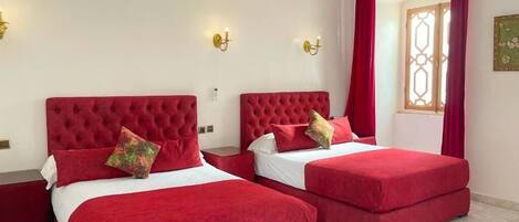 A hotel room with two red beds, white linens, and red curtains.
