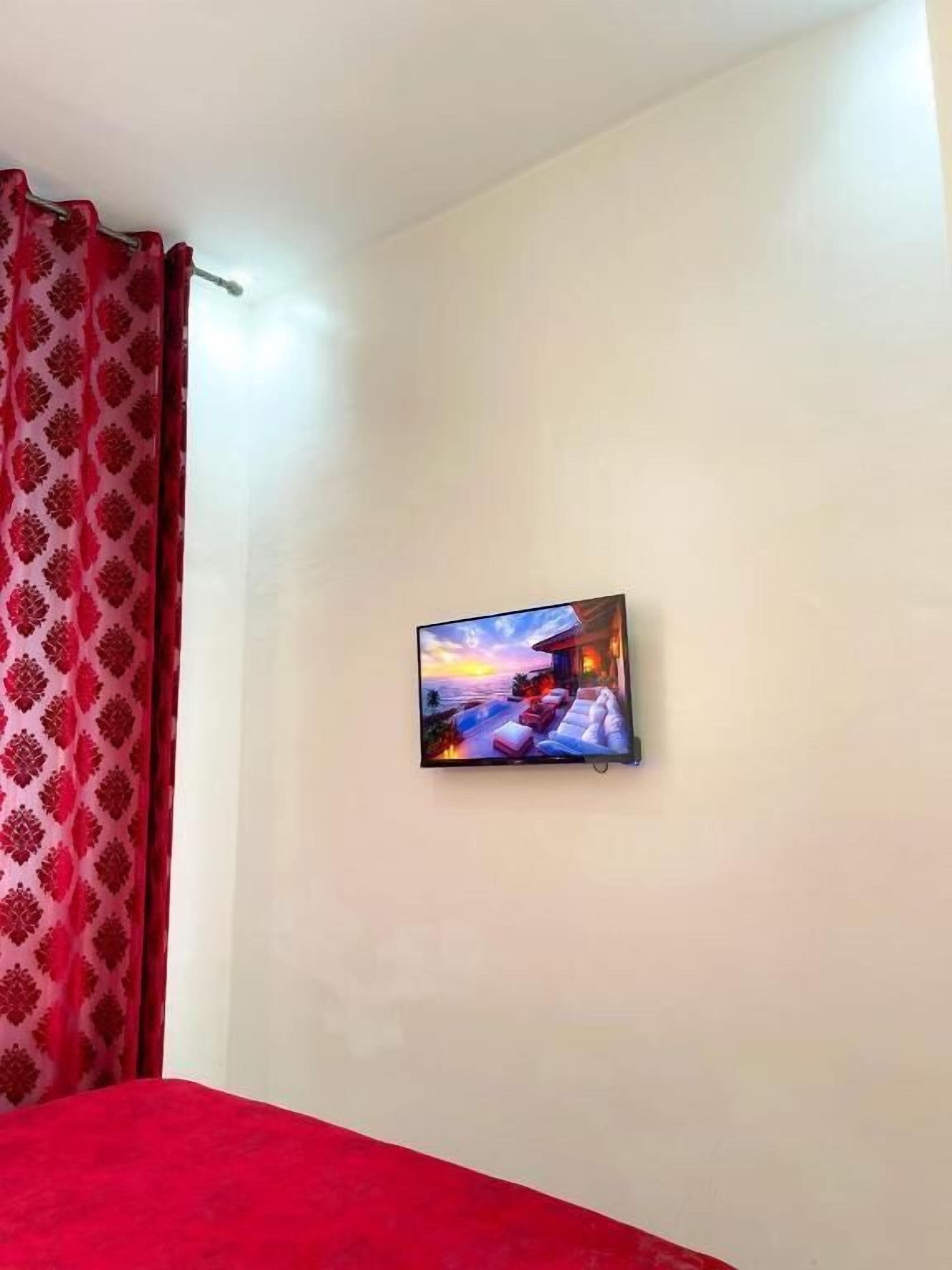 A room with a bed, a wall-mounted TV, and a red curtain.