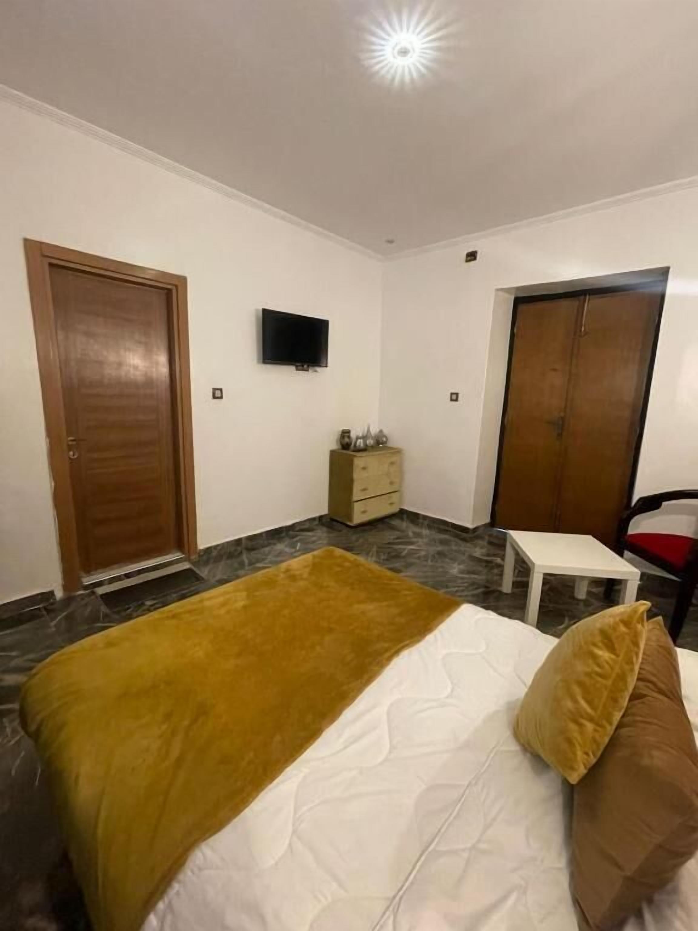 A bedroom with a bed, a television, a wardrobe, and a small table.