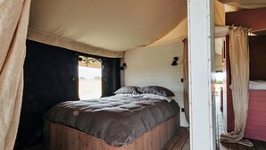 A single bed with a wooden frame and a dark-colored mattress in a tent-like room with white walls and a wooden floor. - Foxley Lodge (Walsingham)