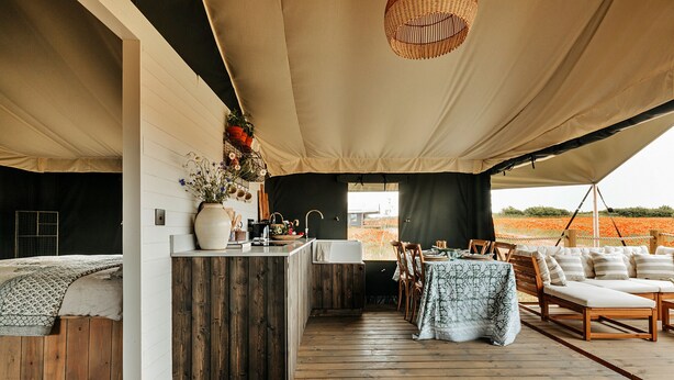 A tented accommodation with a wooden deck, a dining area with a table and chairs, and a cozy seating area with cushions. - Owls Nest (Walsingham)