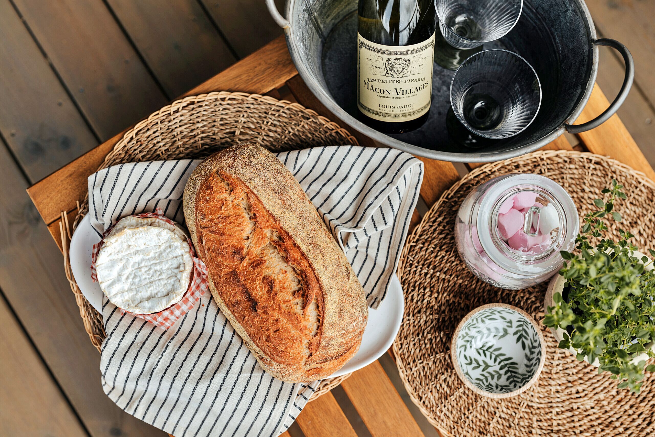 A table with a loaf of bread, a bottle of wine, and a glass jar with pink items.