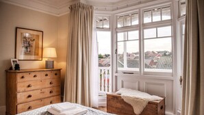 A bedroom with a bed, a wooden dresser, a lamp, a framed picture, and a window with curtains. - Spacious Edwardian 5-bed House, steps from Beach (Kent)