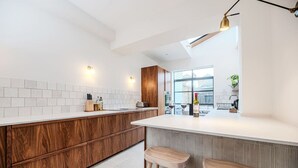 A modern kitchen with a white countertop, wooden cabinets, and a bar area with stools. - Spacious Edwardian 5-bed House, steps from Beach (Kent)