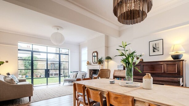 A spacious living room with a large wooden dining table, comfortable seating, and a view of the garden through large windows. - Spacious Edwardian 5-bed House, steps from Beach (Kent)