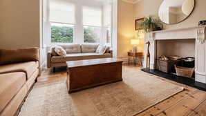 A living room with a sofa, a wooden coffee table, a fireplace, and a large window with blinds. - Spacious Edwardian 5-bed House, steps from Beach (Kent)