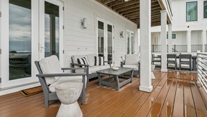 Un'area esterna coperta con pareti bianche, pavimento in legno e arredi tra cui un divano, sedie e un tavolo.