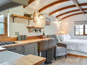 Une cuisine chaleureuse avec des poutres en bois, un coin bar et un lit recouvert d’une courtepointe à motifs floraux.