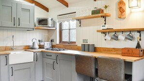 A kitchen with grey cabinets, a microwave, a gas stove, a sink, and a window with a view of trees. - 1 bedroom accommodation in Pocklington (Pocklington)