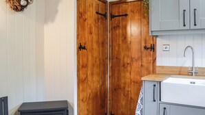 A cozy room with a wood-burning stove, a wooden door, and a kitchen area with cabinets and a sink. - 1 bedroom accommodation in Pocklington (Pocklington)