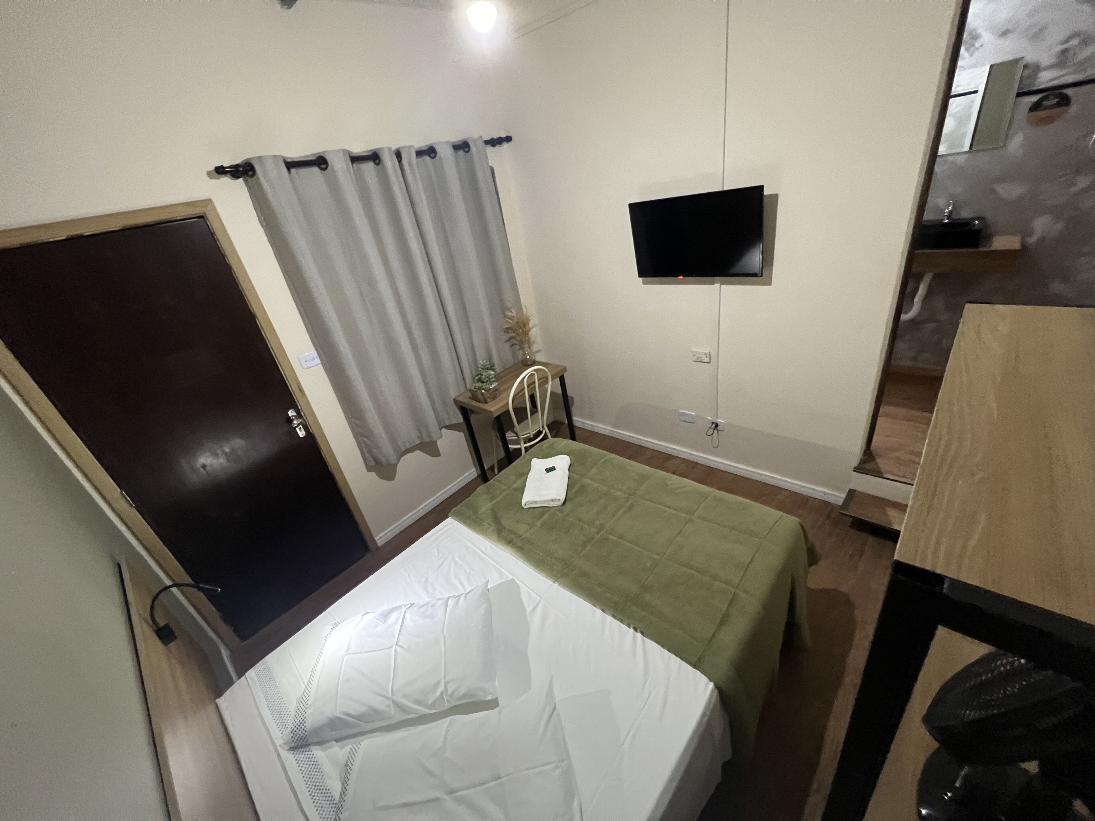 Un dormitorio con una cama, un escritorio, una silla, un televisor y una puerta.