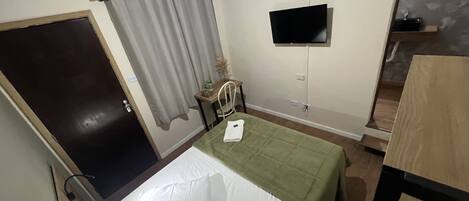 Un dormitorio con una cama, un escritorio, una silla, un televisor y una puerta.