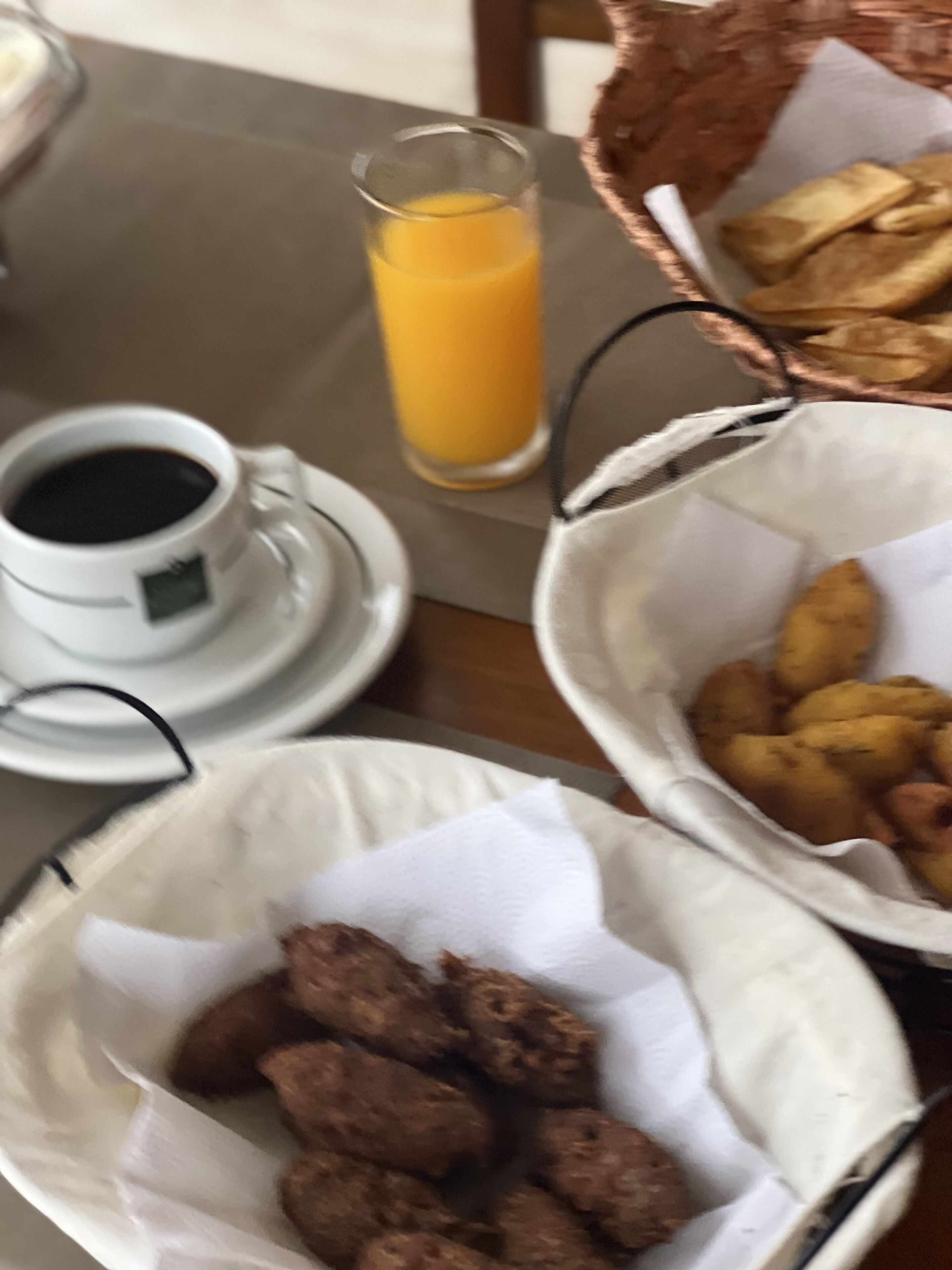 Una mesa con una taza de café, un vaso de zumo de naranja y dos cestas con alimentos.