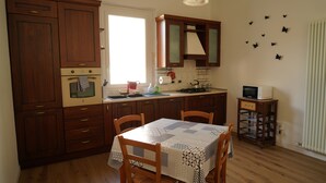 Una cocina con armarios de madera, una mesa con mantel, sillas, un microondas y un carrito pequeño.