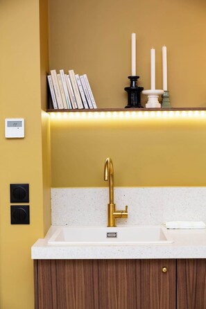 Cozinha moderna com torneira dourada, bancada branca e prateleira com livros e velas.