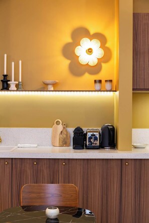 Una cocina con encimera de madera, una máquina de café, una tabla de cortar y una lámpara con forma de flor.