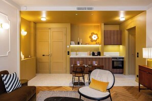 Un espacio habitable compacto con kitchenette, comedor y zona de estar con sofá y sillones.
